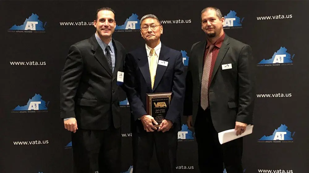 three men smiling, one holding award plaque