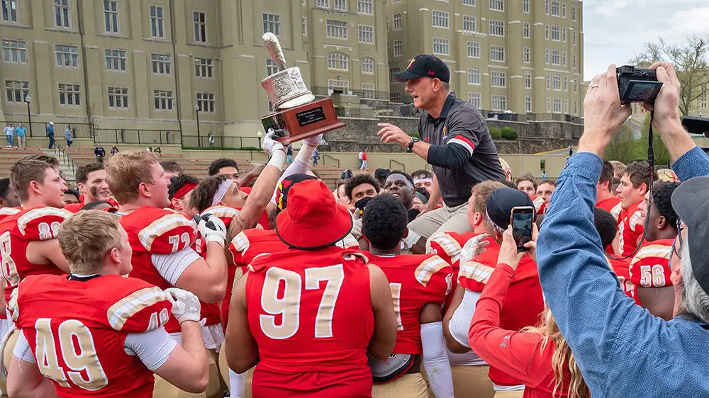 football team hoisting Coach Wachenheim on their shoulders and holding silver shako trophy