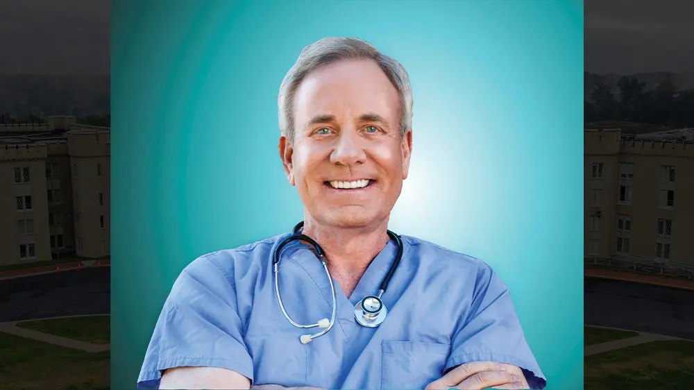 Dr. Slay posing with arms crossed, wearing medical scrubs and stethoscope around his neck.