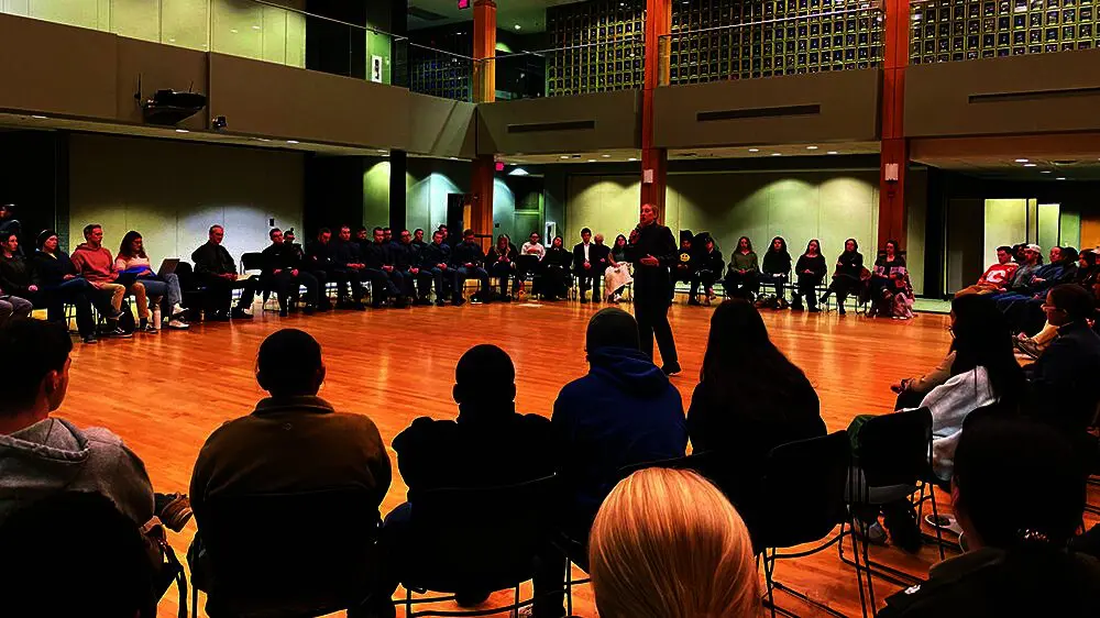 female cadet speaking into a microphone with audience seated in a circle around her