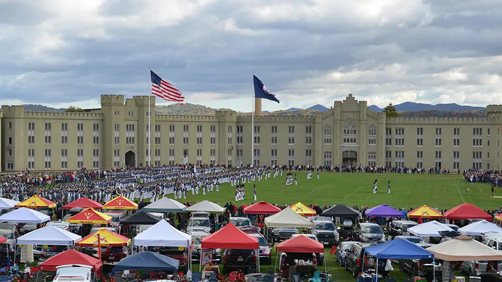 wide shot of old barracks with parade flats up, Corps during parade, and tailgate tents in foreground