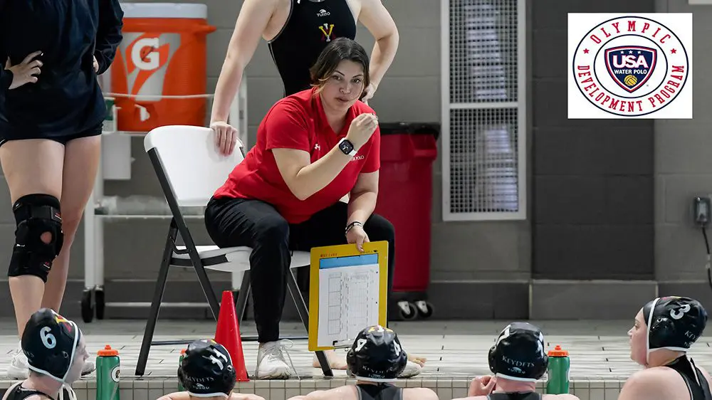 Coach Danielle Montenegro sitting beside pool and giving instructions to water polo team