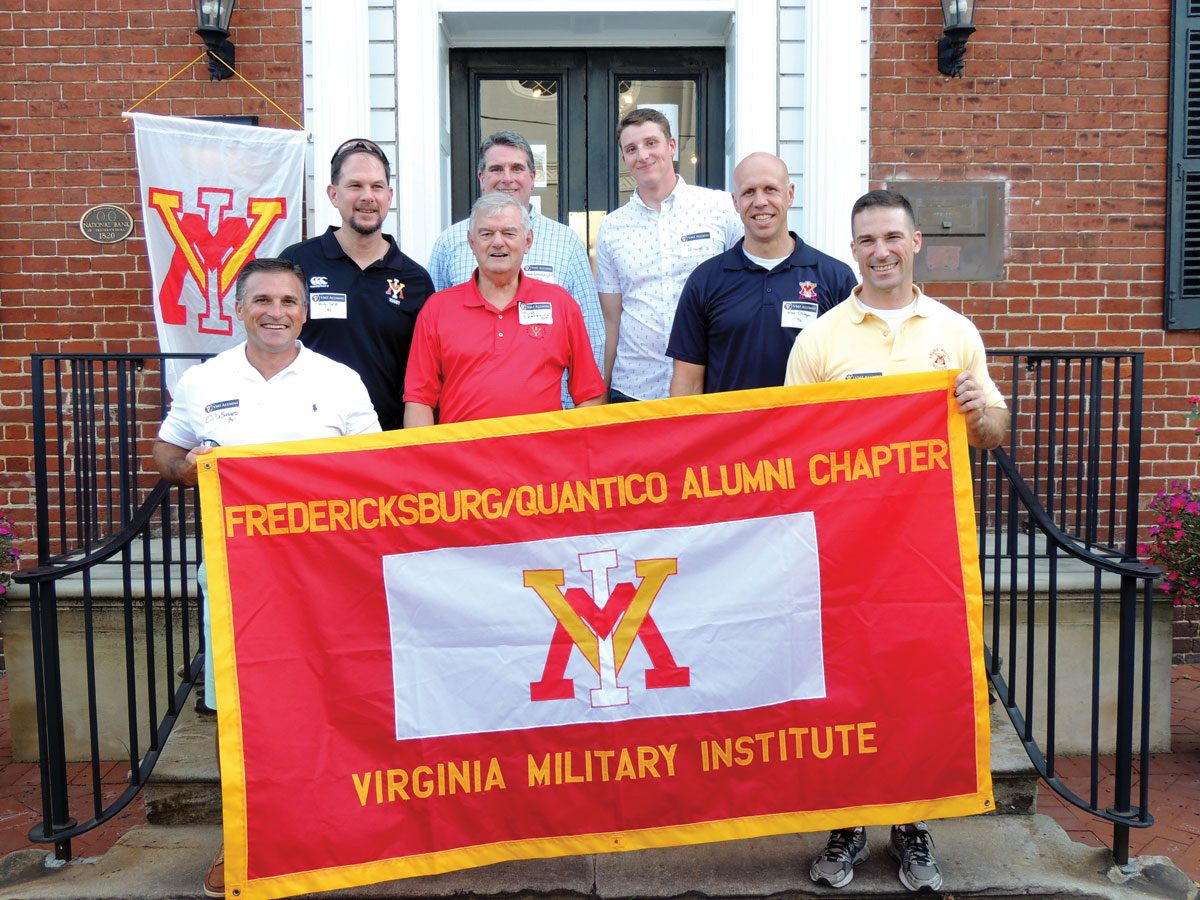 alumni holding vmi flag in front of brick building