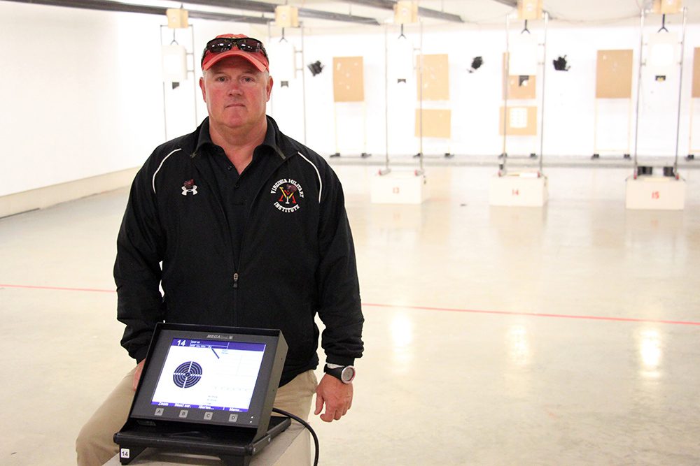 Rifle coach posing behind small monitor.