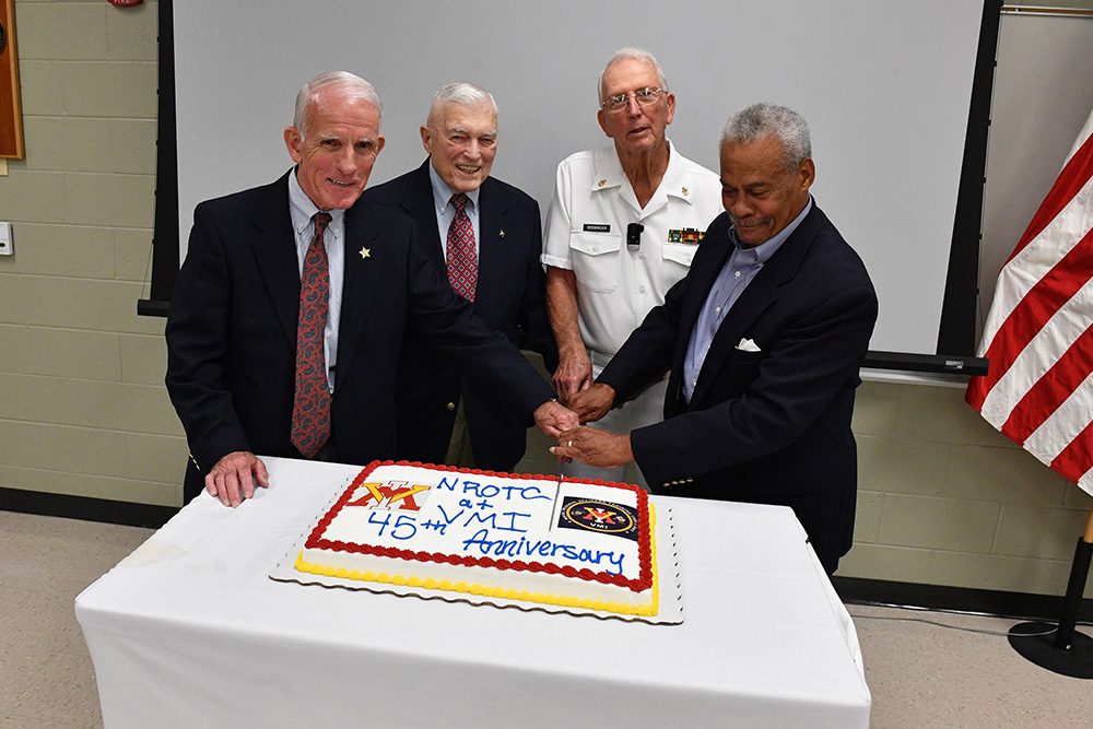Four men smile and post as one cuts a cake for the NROTC 45th anniversary