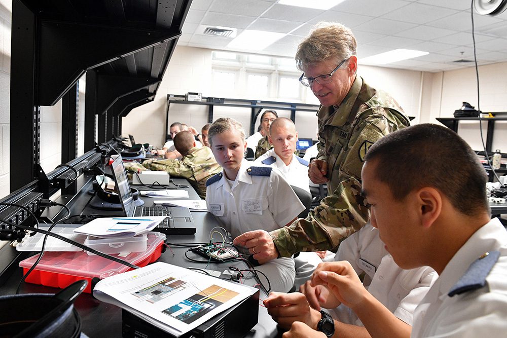 Cadets look as professor points to and explains mechanics in a lab