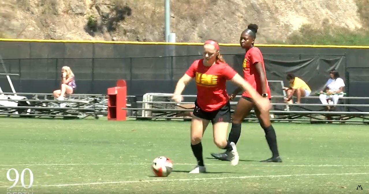 two female VMI soccer players on field, one preparing to kick soccer ball