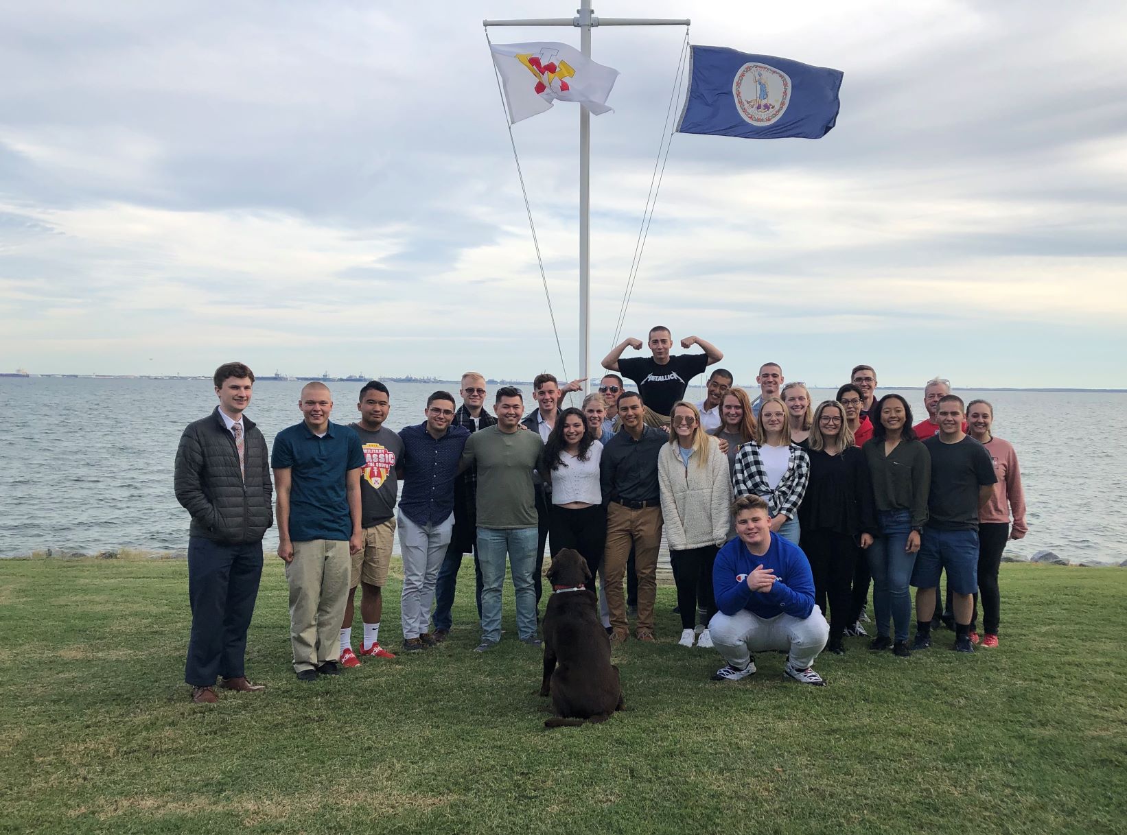 Group of people pose smiling in front of VMI and Virginia flags.