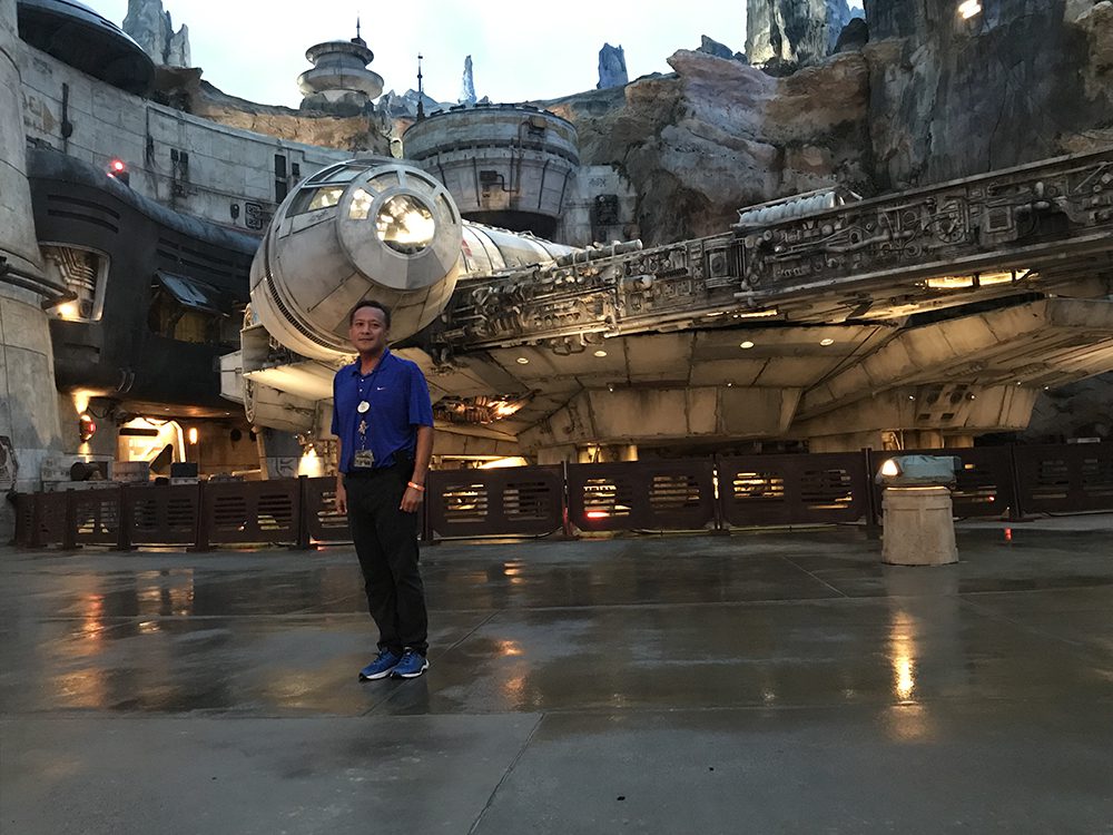 Man standing in front of Millennium Falcon amusement park ride, smiling.