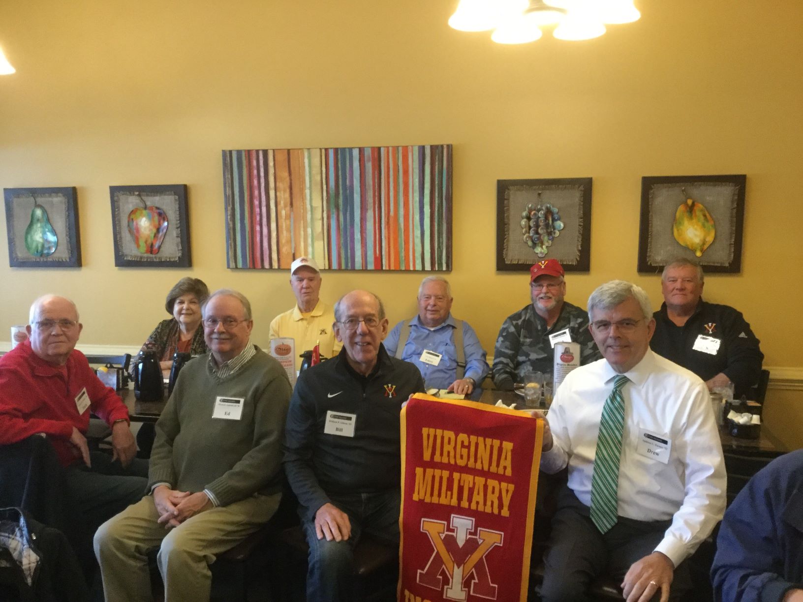 Group of people seated, holding VMI flag, smiling.