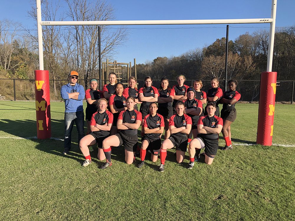 Women's rugby team posing with arms crossed on the playing field