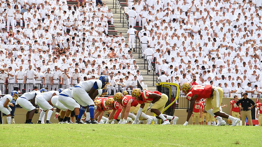 football players on field with cadets in the background