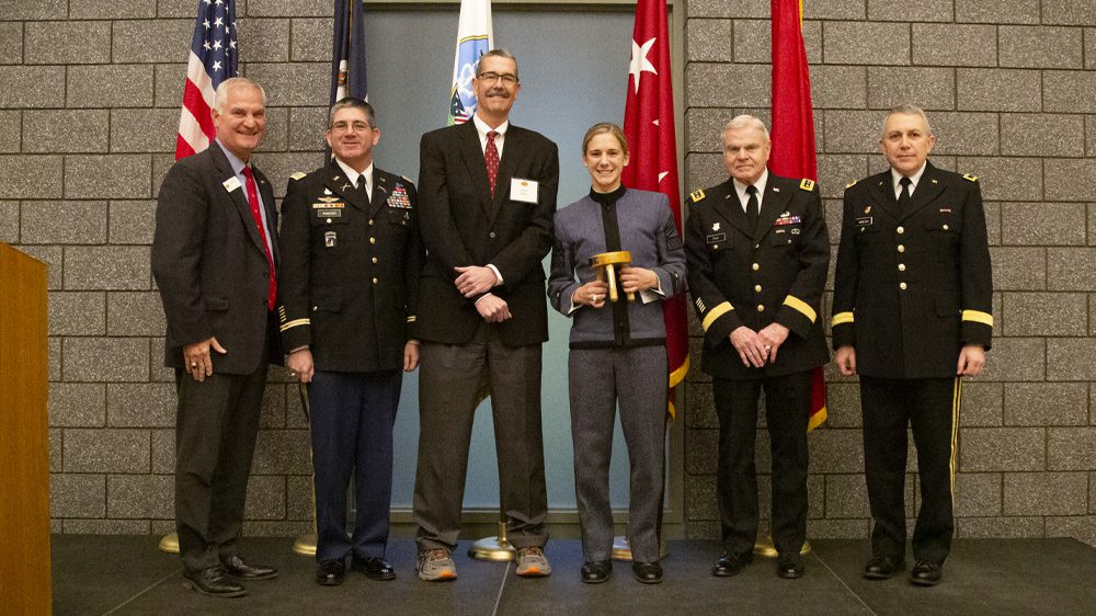 one cadet holding three-legged-stool award and five men stand smiling