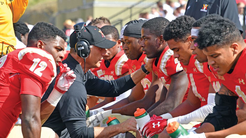 Coach Scott Wachenheim talks to a member of the football team while other members are seated around them