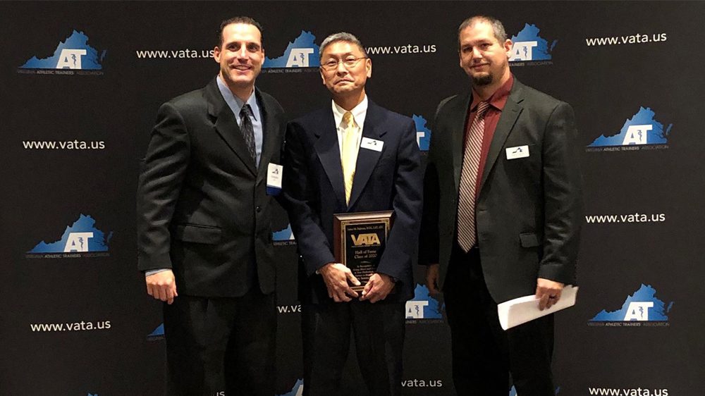 three men smiling, one holding award plaque