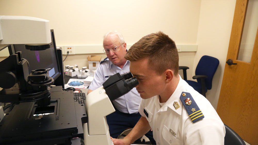 cadet looking through microscope seated next to professor