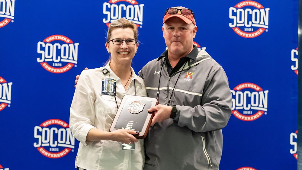 two people stand holding an award plaque in front of SoCon logo background