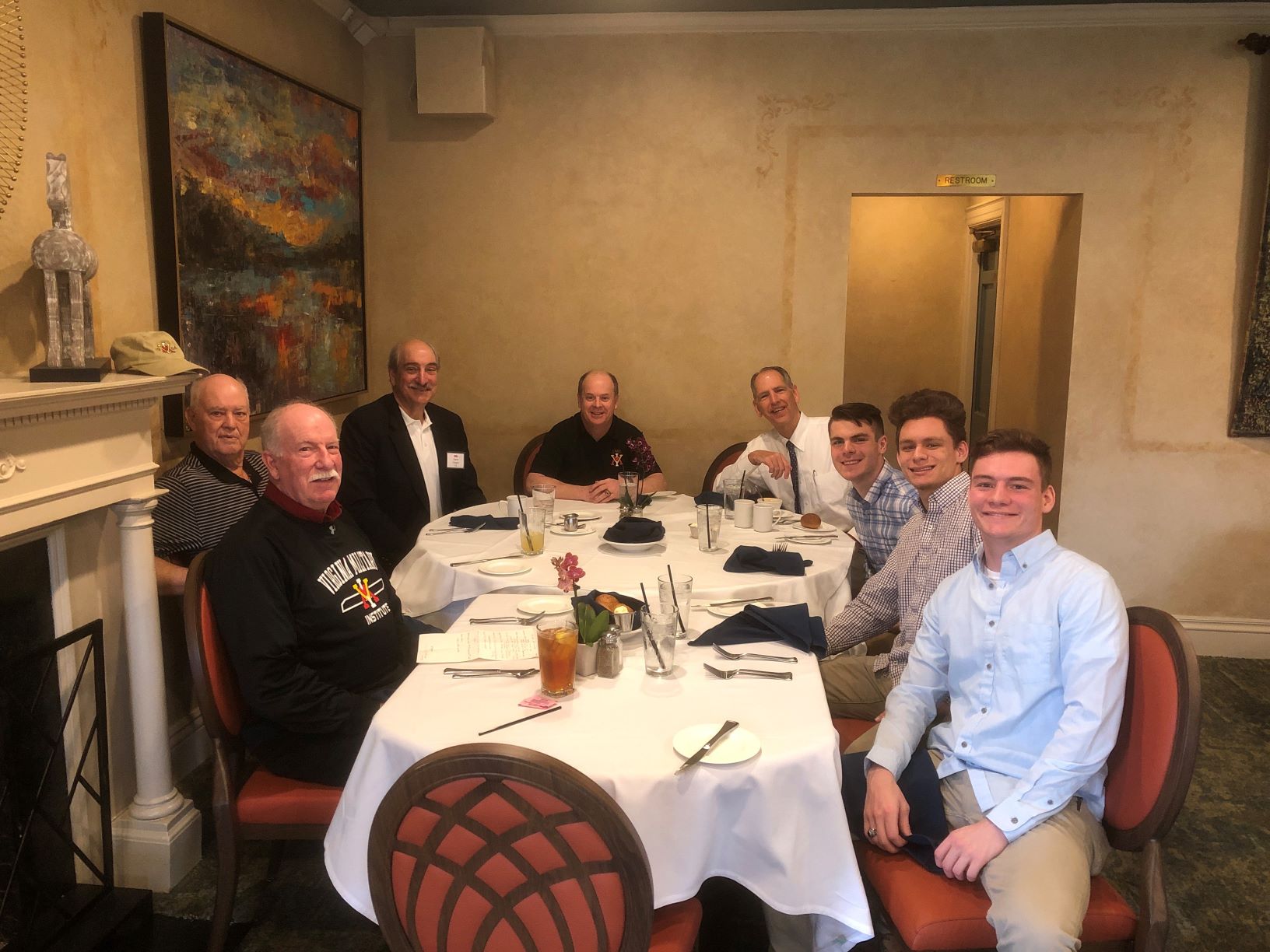 Group of men seated around a dining table, smiling.