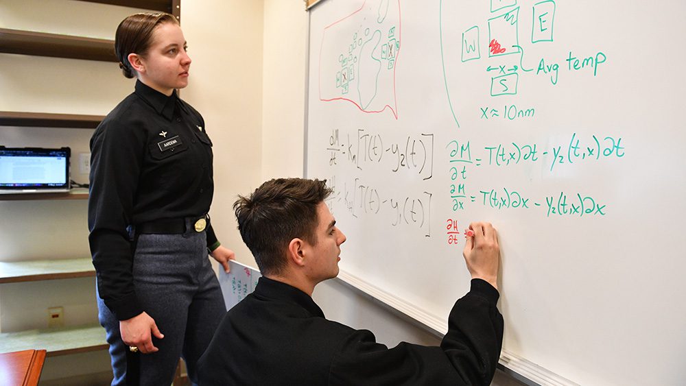 one cadet writes on white board and another looks at what is on board