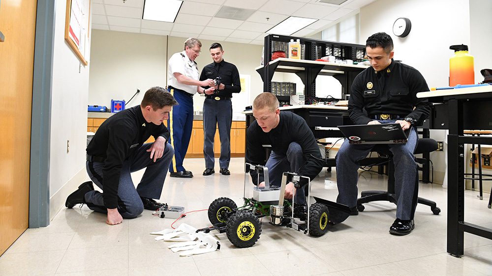 two cadets gather around tick rover as one sits and works on laptop
