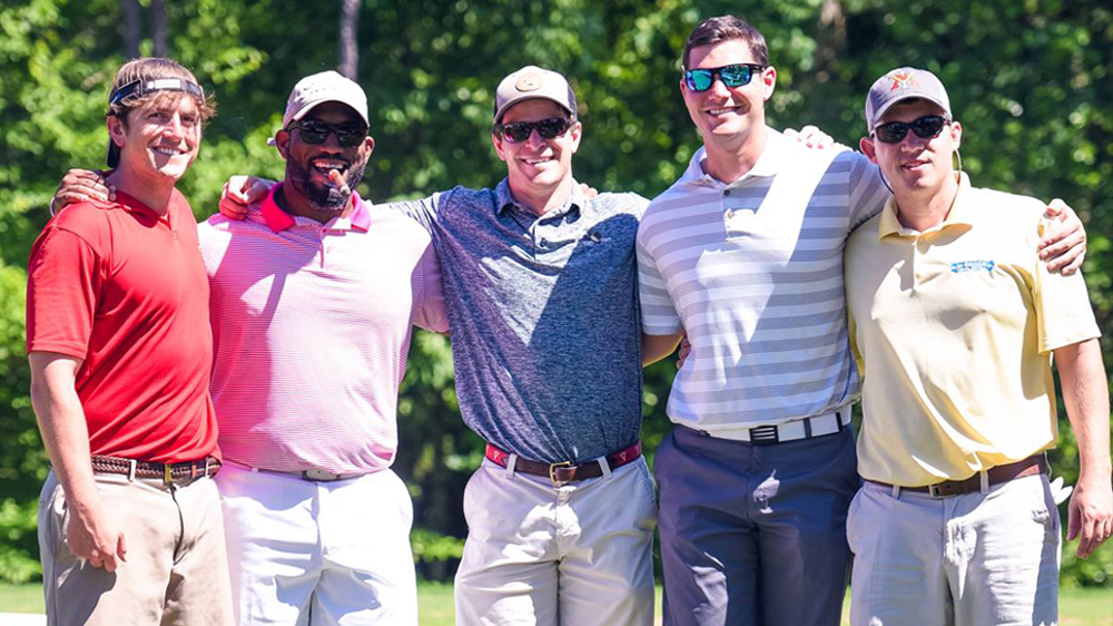 five men pose with arms around each other, smiling