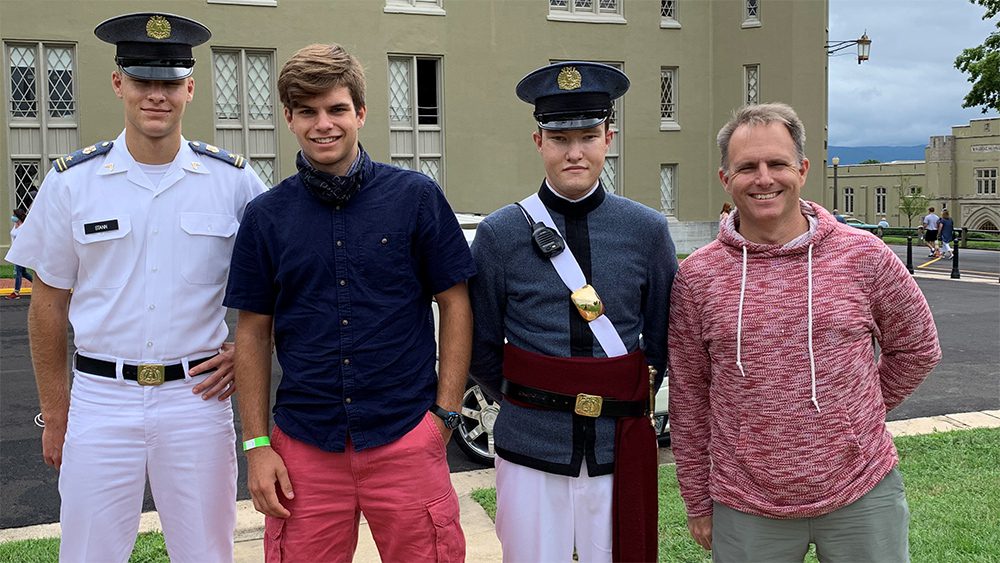 four people, two of whom are cadets, stand smiling