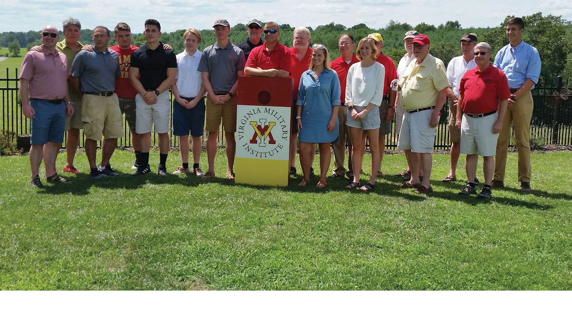 Group of men and women pose with VMI cornhole board, smiling.