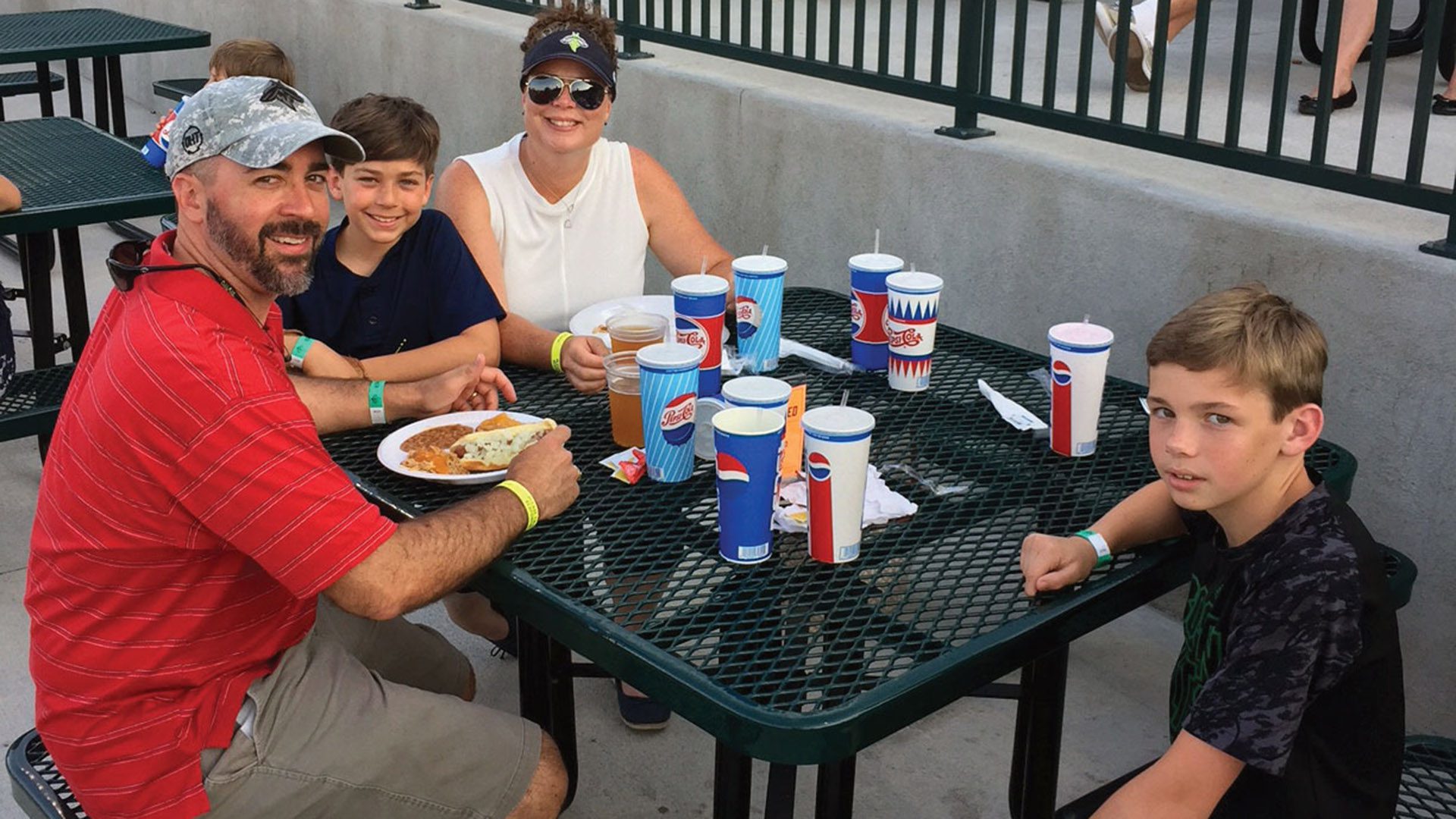 Man, woman, and two young boys seated at outdoor table, eating and smiling.