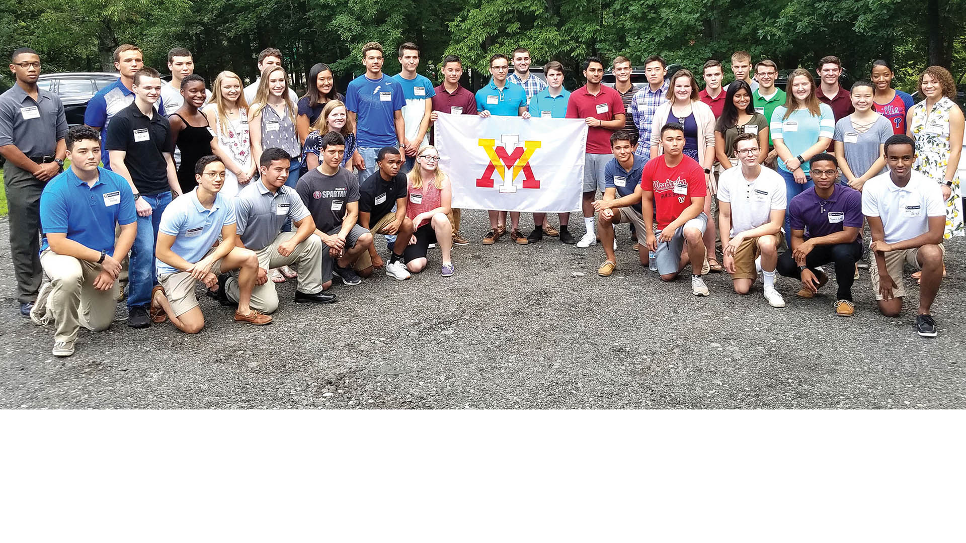 Group of men and women holding up a VMI flag and smiling.