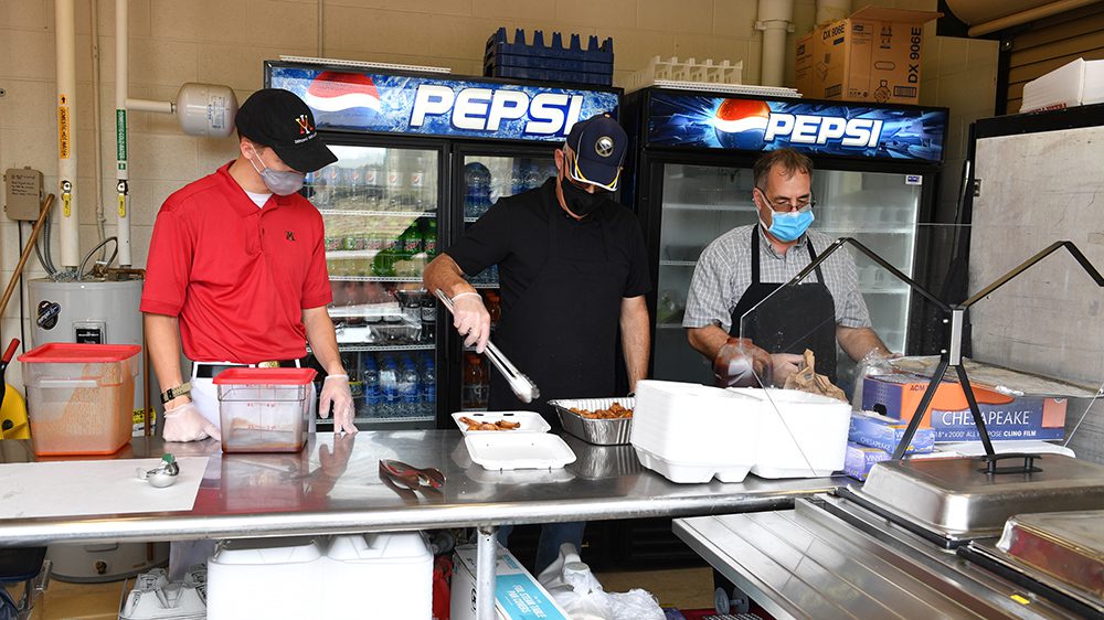 three people stand behind counter putting food in a to go box