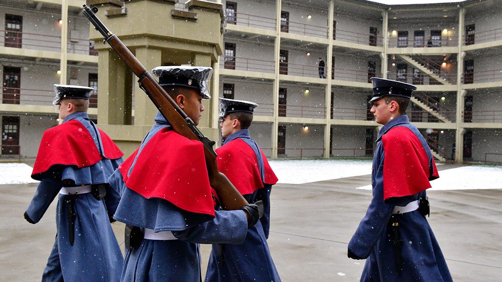 Cadets in winter capes on guard duty, walking near sentinel box.