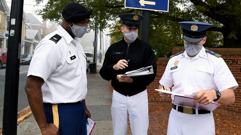 two cadets and a professor review information on a clipboard