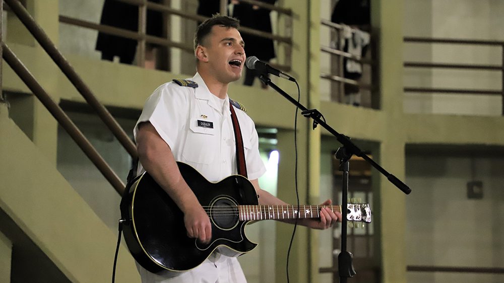 cadet playing guitar and singing into microphone