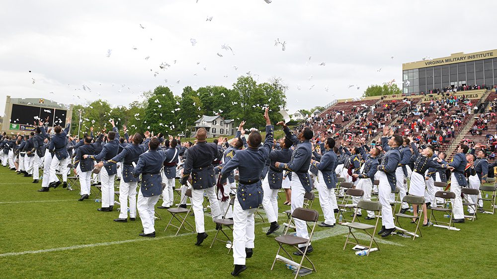 cadets throwing gloves in air at outdoor graduation ceremony