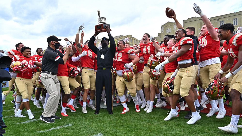 Maj. Gen. Cedric Wins '85 holding silver shako trophy, surrounded by cheering football team