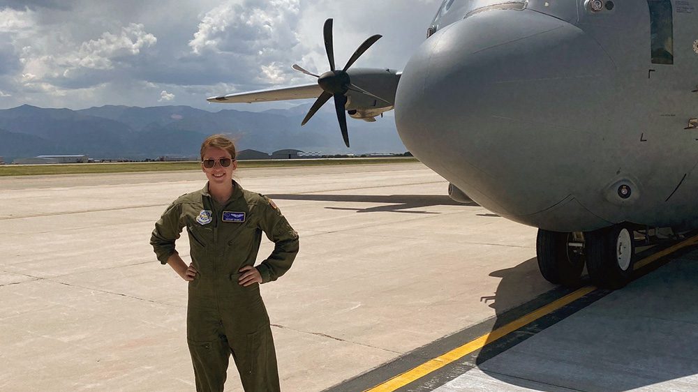 Pilot posing in front of aircraft with hands on hips, smiling.