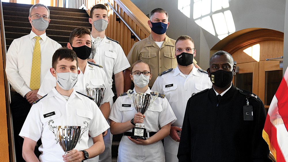 Maj. Gen. Cedric Wins posing with Ethics Team members while two cadets hold trophies.