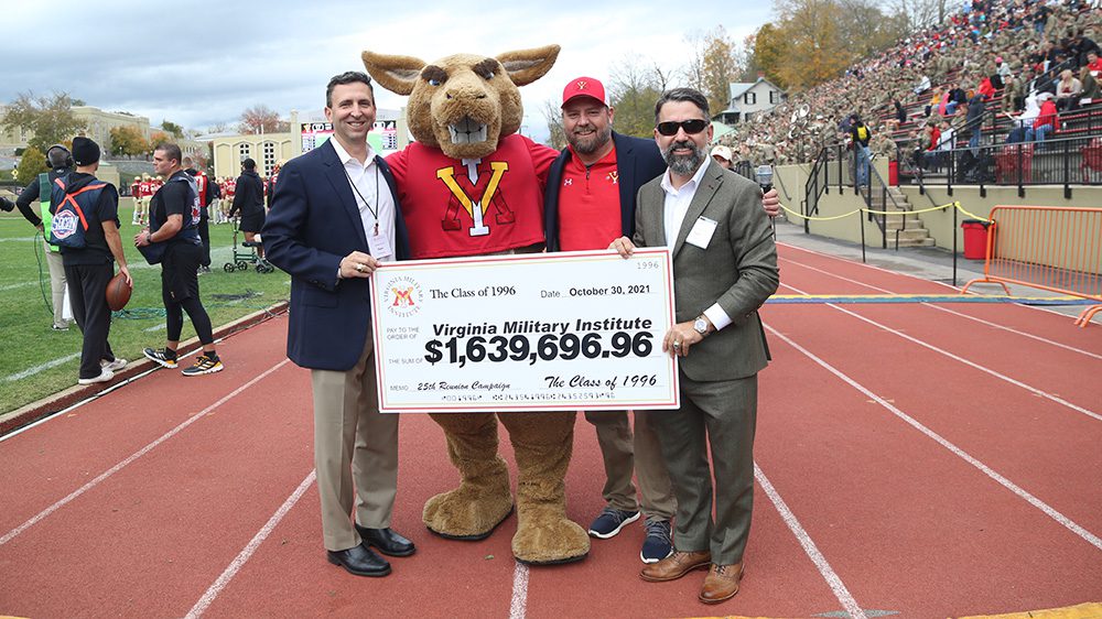 three men pose with Moe and hold giant check to Institute from Class of 1996