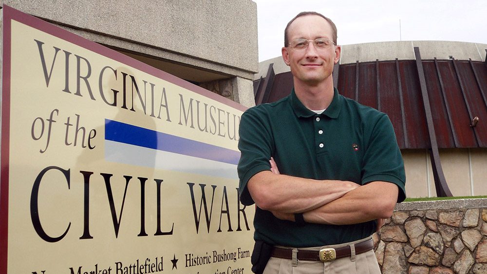 Troy Marshall stands in front of Virginia Museum of the Civil War sign, smiling with arms crossed.