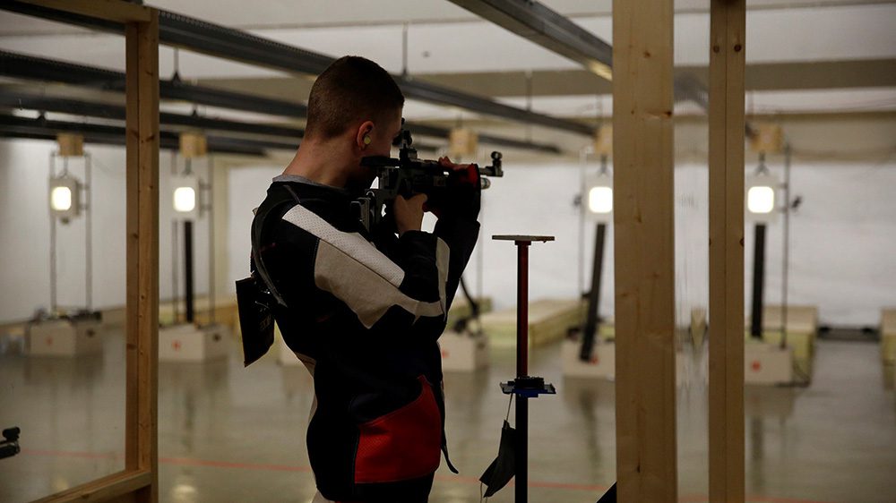 Rifle team member aiming rifle at target.
