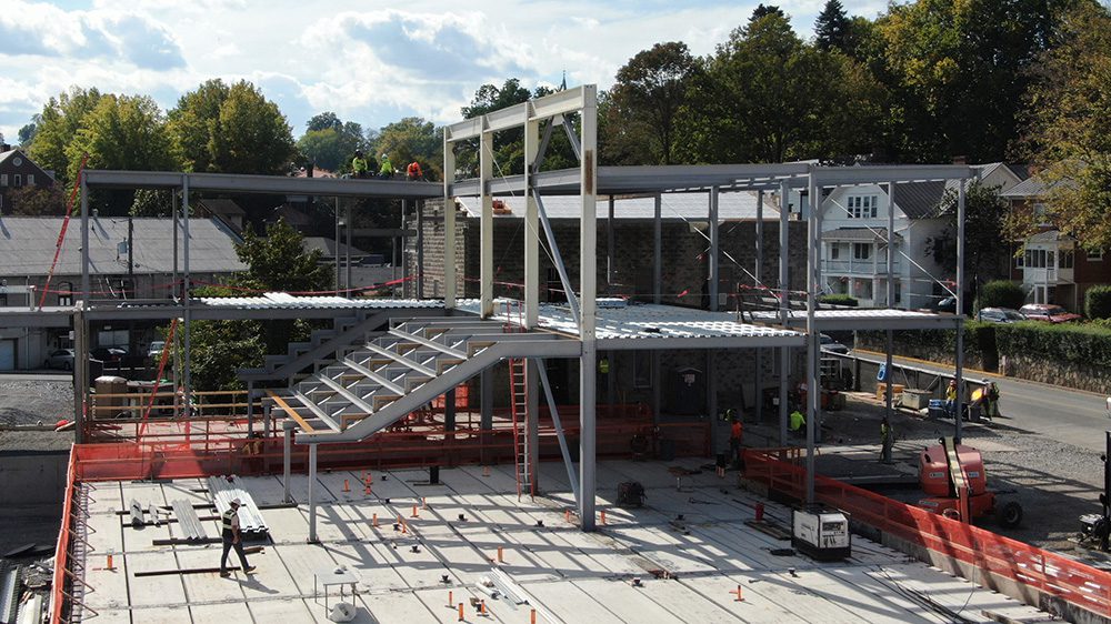 Construction workers walk beneath a steel frame that sits on top of a concrete base.