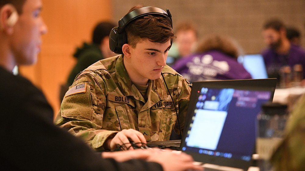 cadet in OCP wearing headphones and working on laptop