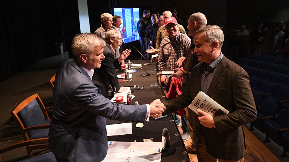 people line a table on both sides, two men shaking hands