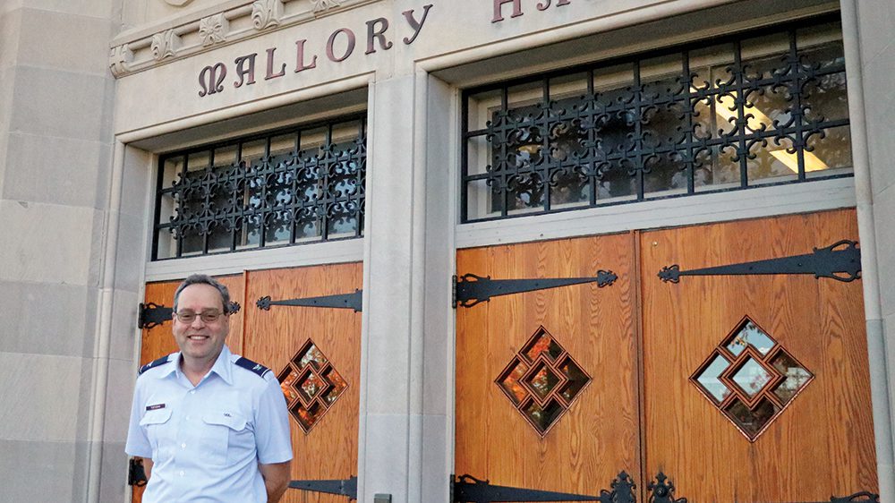 Col. Greg Topasna in front of Mallory Hall, smiling.