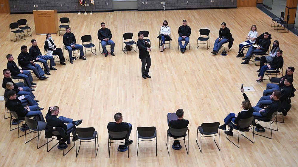 Participants sit in chairs arranged in a circle, as representatives from the Braver Angels organization facilitate a civil debate in the Hall of Valor in Marshall Hall.