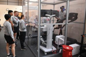 One cadet runs on treadmill in altitude chamber, while four other cadets observe.