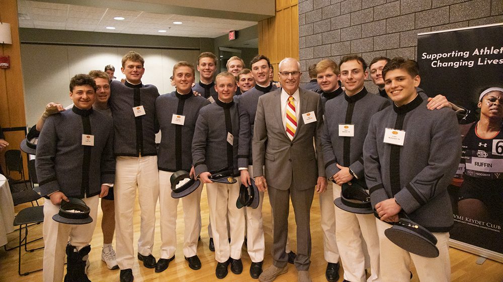 Group of Cadets and an alumnus stand with arms around each other, smiling