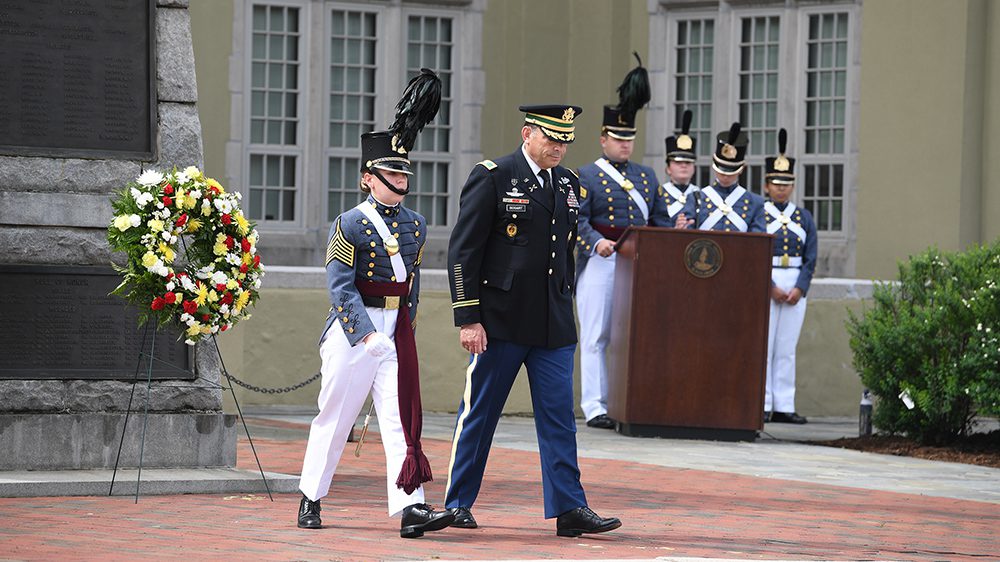 Four cadets stand behind a podium; Kasey Meredith '22 and Col. Adrian Bogart '81 stand in front of Virginia Mourning Her Dead statue and wreath