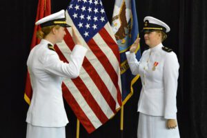 Christina Skaggs ’22 commissions into the U.S. Navy, with right hand raised, in front of American flag.