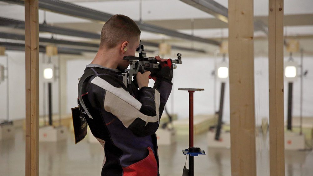 Rifle team member aiming rifle at target.